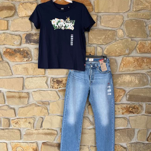 Navy T-shirt with floral LEVIs graphic paired with light blue jeans hangs on a stone wall. Casual and stylish vibe with earthy tones.