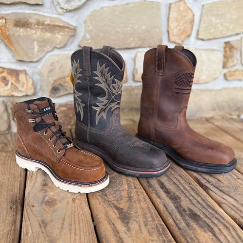 Three cowboy boots on a wooden floor in front of a stone wall. Each boot has a distinct style and color, conveying a rustic and rugged tone.
