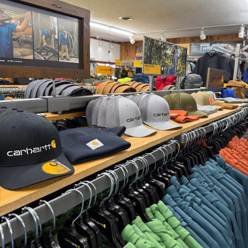 Carhartt retail display with branded caps, beanies, jackets, and colorful clothing on racks; rugged outdoor-workwear store atmosphere.