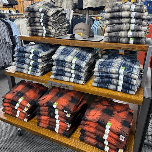 Retail store display stacked with blue, gray, and orange plaid shirts on wooden shelves, creating a neat, colorful outdoor apparel selection.