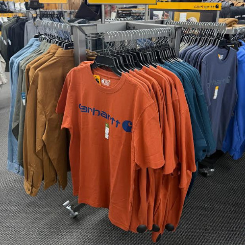 Retail clothing rack displaying Carhartt T-shirts in orange, brown, teal, gray, and blue, creating a busy but organized store atmosphere.