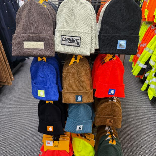 Colorful Carhartt knit beanies hang on a store rack, featuring black, gray, blue, brown, red, and neon safety-workwear colors.