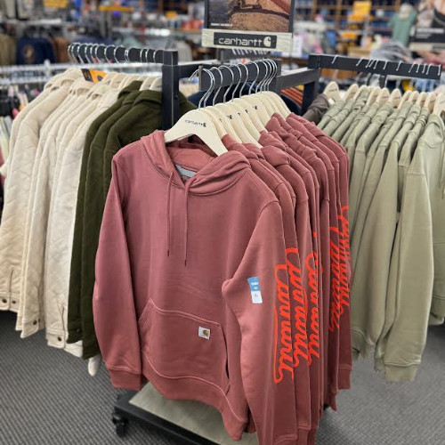 Retail clothing rack filled with Carhartt hoodies in dusty pink, cream, olive, and sage green, creating a casual, cozy store display.