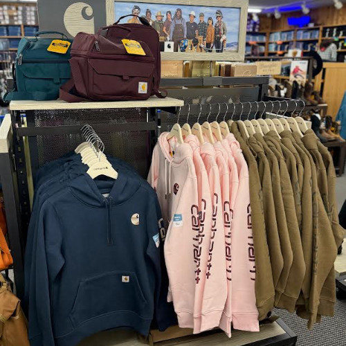 Retail clothing display with backpacks on a shelf and rows of navy, pink, and olive hoodies in a well-lit store, creating a casual tone.